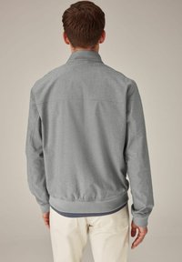 Chaqueta bomber gris con una textura sutil, puños y dobladillo acanalados. Cuenta con un cuello clásico y una cinturilla elástica, usada sobre pantalones de color claro.
