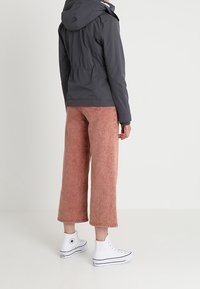 Szara kurtka z kapturem, różowe spodnie o szerokich nogawkach sięgające krócej i białe trampki. Strój cechuje się casualowym stylem, miękką fakturą i stonowanymi kolorami.