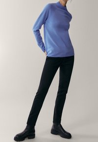 Pull bleu clair à manches longues avec un col haut, associé à un jean noir ajusté et des bottines noires à semelles épaisses.