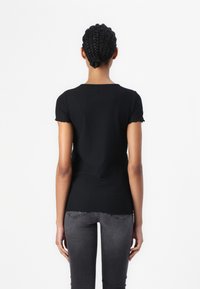 Mustat ribattu lyhythihaiset paidat, joissa on pyöreä kaula-aukko ja hieman röyhelömäiset hihat, yhdistettyinä tiukkoihin tummanharmaisiin farkkuihin.