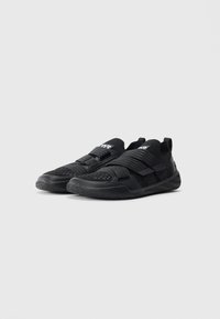 Black athletic shoes with textured soles, mesh upper, wide elastic strap, and branded tongue logos placed side by side on gray background.
