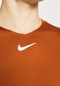 Nike sportströja i stark orange, med en v-ringning och vit logotyp. Materialet verkar lätt med en texturerad yta.