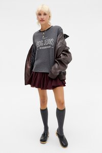 Pruhované sivé a čierne tričko s textom, hnedá kožená bunda, bordová károvaná sukňa, sivé ponožky po kolená a čierne kroksy.