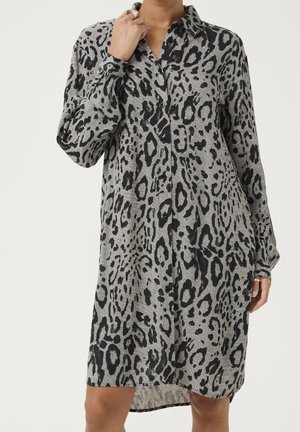 Femme portant une robe grise ample avec un imprimé léopard noir, des manches longues, un col et des boutons sur le devant.