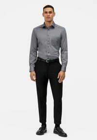 Camicia grigia con bottoni, dotata di tasca, abbinata a pantaloni neri su misura e scarpe nere. Tessuto liscio, design aderente e colletto classico.
