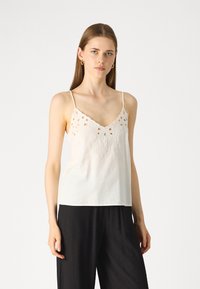 Camisole en coton blanc avec un motif découpé décoratif et une broderie florale au niveau du col. Fines bretelles et coupe décontractée.