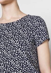 Námořnická blůza s kulatým výstřihem a krátkými rukávy, zdobená bílou tečkovanou vzorem, vyrobená z hladkého, lehkého materiálu.