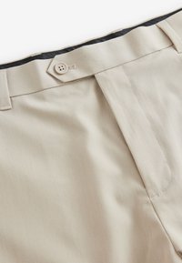 Pantalon beige avec braguette zippée, fermeture par un seul bouton, texture de tissu élégante et détails de couture subtils le long des coutures.