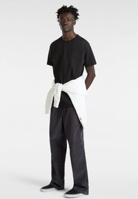 T-shirt en coton noir avec un col rond, associé à un pantalon en velours côtelé gris et un sweat-shirt blanc noué à la taille. Chaussures noires à enfiler.