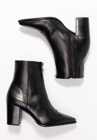 Par de botines de cuero negro con tacones de bloque y cremalleras laterales sobre un fondo blanco.