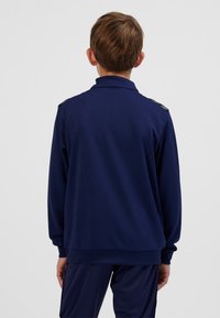 Mörkblå sportjacka i texturerat tyg. Har en ståkrage och axeldetaljer. Långa ärmar och muddade ärmslut.