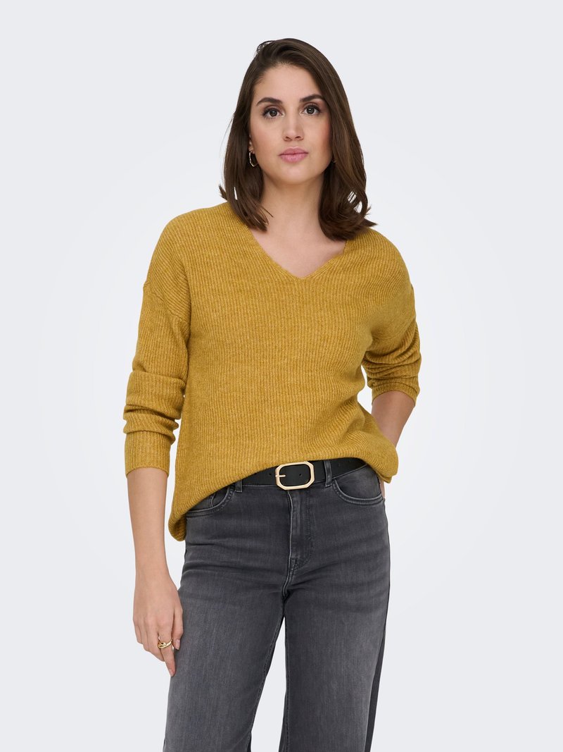 Senfgelber, gerippter Strickpullover mit V-Ausschnitt, lockerer Passform und hochgekrempelten Ärmeln. Kombiniert mit dunkelgrauen Jeans und einem schwarzen Gürtel.