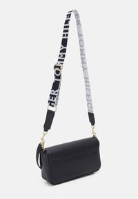 Sac bandoulière rectangulaire noir avec une large sangle ajustable en noir et blanc, comportant le nom de la marque.