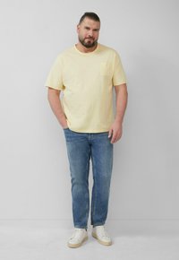 Geel katoenen T-shirt met korte mouwen en een borstzak, gecombineerd met blauwe spijkerbroeken en witte sneakers. Eenvoudige, casual stijl.