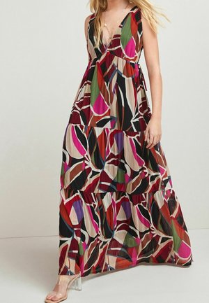 Frau trägt ein ärmelloses, maxi-langes Kleid mit mehrfarbigem, abstraktem Druck, tiefem V-Ausschnitt und gestuftem Rock, kombiniert mit Sandalen mit klarem Absatz.