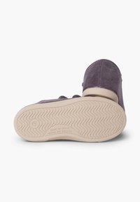 Chaussure en velours côtelé violet avec une semelle en caoutchouc présentant un motif de semelle ondulé. Détails surpiqués dans la partie supérieure, marquée "Fabriqué en Espagne."