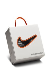 Pakiranje Nike Swoosh 1, bijela kutija s narančastom drškom, sadrži izrez u obliku dizajna cipela koji otkriva crni materijal i bijele akcentne detalje.