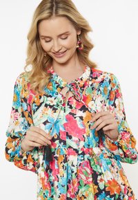 Blumenkleid mit mehrfarbigen Mustern auf schwarzem Hintergrund, mit einer Schleife am Hals, Puffärmeln und Quastendetail am Ausschnitt.