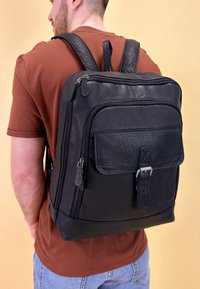 Zaino in pelle nera con tasca frontale, doppia cerniera e spallacci regolabili. Superficie testurizzata con un design elegante e moderno.