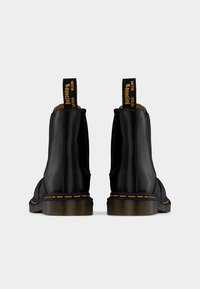 Botas de cano curto em couro preto com costura amarela, painéis laterais elásticos e uma aba de puxar com o texto "WITH SOLES" em amarelo no topo.