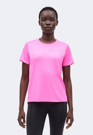 Naine seisab, kandes erkroosa lühikeste varrukatega sportlikku särki ja musti kitsaid pükse, suunaga ettepoole ning neutraalse ilmega.