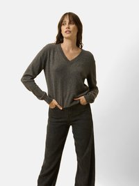 Maglione grigio a scollo a V in morbido tessuto con polsini a coste. Abbinato a jeans neri a gamba larga a vita alta. Tessuto liscio, vestibilità rilassata.