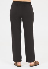 Schwarze, weiche Stoffhosen mit einem elastischen Bund; verfügen über ein gerades Bein Design und seitliche Taschen. Getragen mit hellbraunen Slippern.