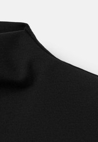 Primo piano di un tessuto nero che mostra un colletto alto con cuciture visibili e un motivo a maglia liscio e leggermente strutturato.