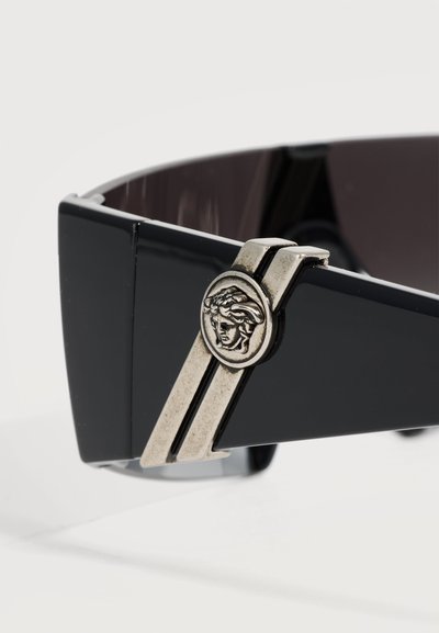Branches de lunettes de soleil noires avec détail en métal argenté présentant un emblème en relief tête de Méduse et des double rayures.