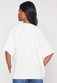 Witte linnen top met een losse pasvorm, kimono-stijl mouwen en een gestructureerde stof. Heeft een geplooide achterkant voor extra detail.