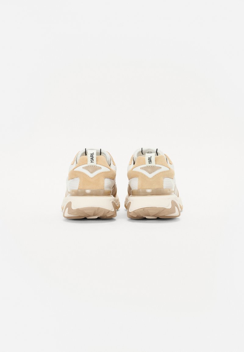 Beige Sneaker mit beigem Wildleder- und Mesh-Obermaterial, runder Form, gepolsterter Kragen und dicke Gummisohle. Rückseite zeigt Branding-Detail.