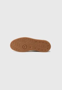 Rubber shoe sole with a textured, wavy pattern, light brown color, and circular accents. The bottom shows grip details and minimal branding.