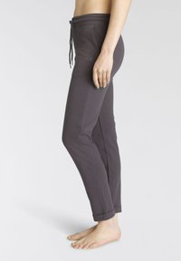 Graue Sweatpants mit einem Kordelzugbund, tailliertem Design, aufgerollten Bündchen und kleinem gesticktem Logo auf dem linken Oberschenkel. Weicher Materialtextur.