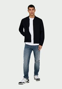 Dark navy bomber jacket with a high collar, paired with a white t-shirt, light blue jeans, and black and white sneakers. Simple design.