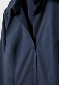 Navy blue button-up shirt made of a smooth, lightweight fabric. Features a classic collar and subtle texture with concealed buttons.