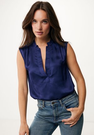 Blouse en soie navy avec un col en V et des épaules plissées, associée à un jean en denim bleu clair taille haute. Texture lisse et coupe décontractée.