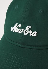 Zöld szövet sapka ívelt viselővel. Fehér hímzett "New Era" logóval rendelkezik. Továbbá varratokkal létrehozott textúra részletekkel és szellőző lyukakkal rendelkezik.