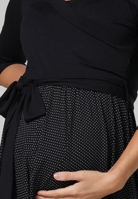 Top negro de estilo envolvente con mangas tres cuartos, combinado con una falda de lunares en blanco y negro. Presenta un detalle de cintura anudada.