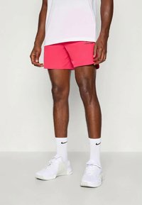 Ružové športové šortky z ľahkého materiálu s logom Nike na boku, doplnené bielymi teniskami a ponožkami.