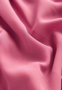 Rosa Stoff mit einer glatten, matten Textur, der sanfte Falten und eine sanfte Drapierung zeigt. Die Webart ist fein und gleichmäßig, wodurch das leichte Erscheinungsbild verstärkt wird.