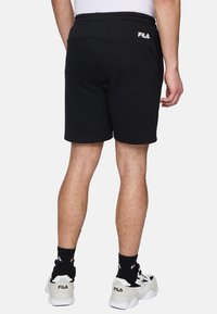 Svarta bomullsbyxor med ett elastiskt midjeband, med subtila sömnadsdetaljer. Kombinerat med vita och grå sneakers samt svarta strumpor.