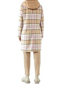 Geruite jas van zachte stof in beige, roze en witte tinten; heeft een puffy, lichtbruine capuchon en effen beige broek met enkelboots.