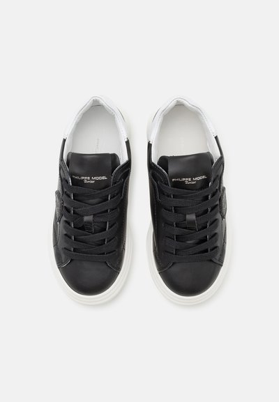 Baskets en cuir noir avec des accents blancs, bout rond, lacets plats et détail texturé sur les côtés. Présente un logo en relief sur la languette.