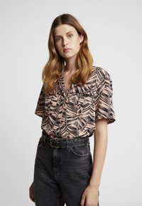 Kortebloemige, button-up blouse in perzik met een zwart bladenpatroon. Gecombineerd met een donkerdenim spijkerbroek en een zwart met studs versierde riem.