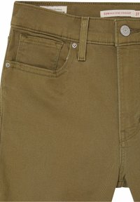 Pantalones rectos de tiro alto, marrones, hechos de una mezcla de algodón. Cuenta con cinco bolsillos, costuras visibles y cierre de botón de metal.