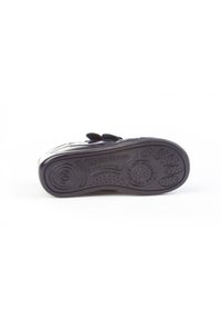 Zapato negro con suela plana que presenta patrones circulares de agarre. Correa de velcro ajustable para un ajuste seguro. Superficie texturizada para mayor comodidad y durabilidad.