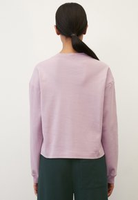 Light purple sweatshirt with a relaxed fit, dropped shoulders, and ribbed cuffs, paired with dark green pants featuring side pockets.