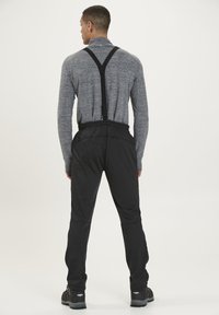 Sorte udendørbukser med justerbare seler, elastisk talje og tapered ben. Bæres med en grå langærmet top.