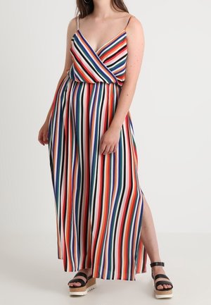 Woman wearing a sleeveless, multicolored vertical striped maxi dress with a v-neck and black platform sandals, standing against a white background.