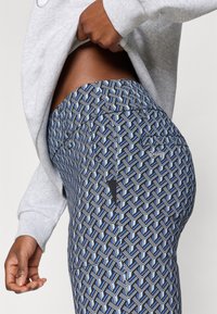 Legingi ar ģeometrisku rakstu zilā, melnā un baltā krāsā, ar augstu jostasvietu un nelielu kabatu detaļu.